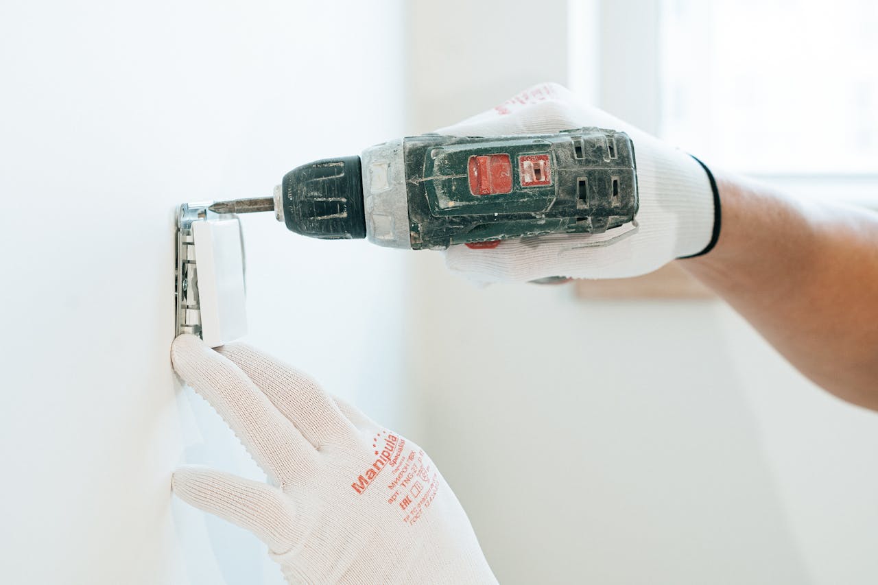 hero-img-02 Gloved hands using a drill to install a power outlet on a wall, focusing on precision and safety.