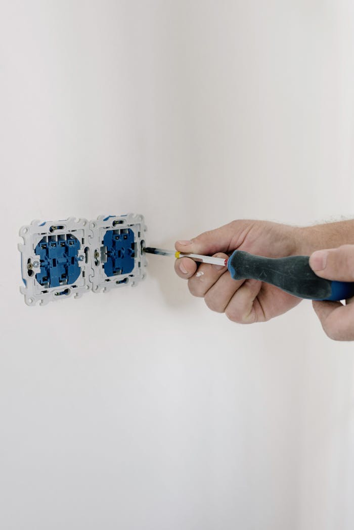 services-01 Close-up of hands using a screwdriver to install electrical sockets on a white wall.